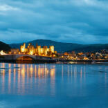 Conwy Castle lit up at night and reflecting in the water.