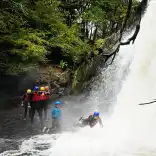 Group of adults with instructors jumping into a waterfall.