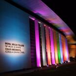 Exterior of a music and drama college at night lit up with colourful lights.