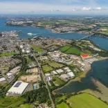 Aerial shot of sea and bridge crossing waterway with lots of businesses set up on green land.