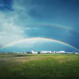 Rainbow over the landing field at airport and white buildings in background.