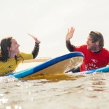 2 people on a surfboard doing a high five.