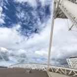 A person ziplining above the roof of a sports stadium.