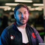 John Jackson sitting talking to camera wearing a blue jacket with red motiff and white tshirt 