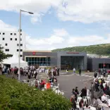 image of foyer exterior of the Trefirest campus with peopole on plastic seats and standing talking