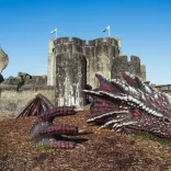 Dragon laying on the floor with thr castle and leaning tower of Caerphilly