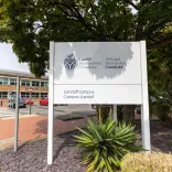 exterior view of Cardiff's Metropolitan University with bilingual welcome sign building in background and trees in the forefront teh university 