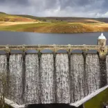 water falling down the dam with lake and mountains behind
