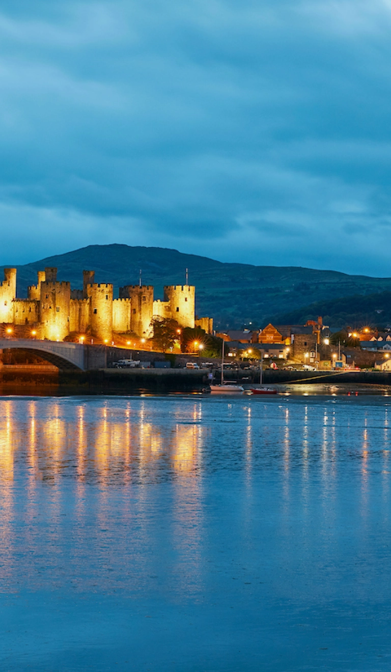 Conwy Castle lit up at night and reflecting in the water.