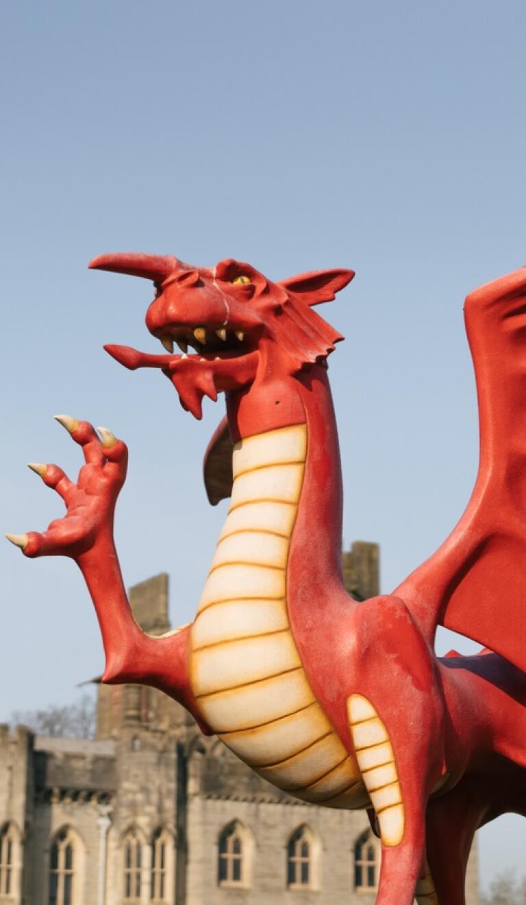 A statue of a Welsh dragon with a castle in the background.