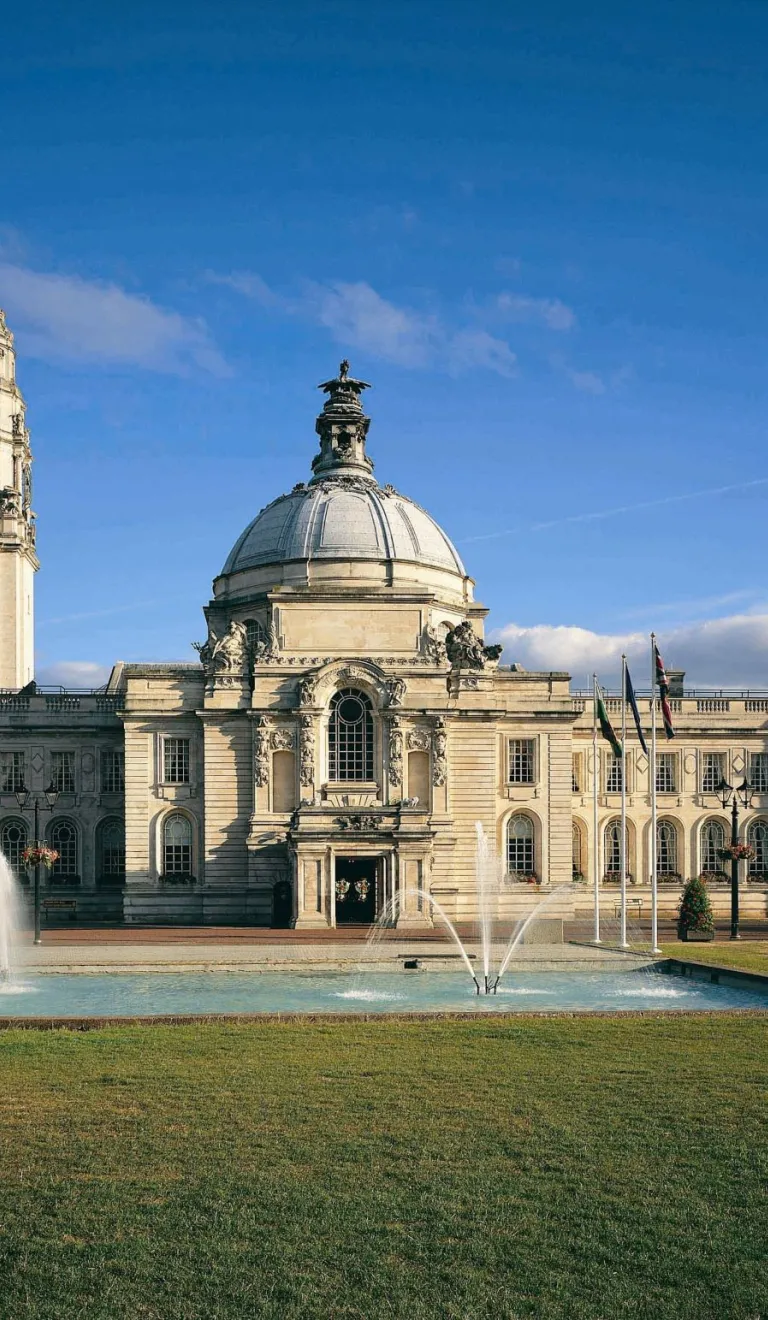 A city hall with a fountain on the lawns at the front of the building.