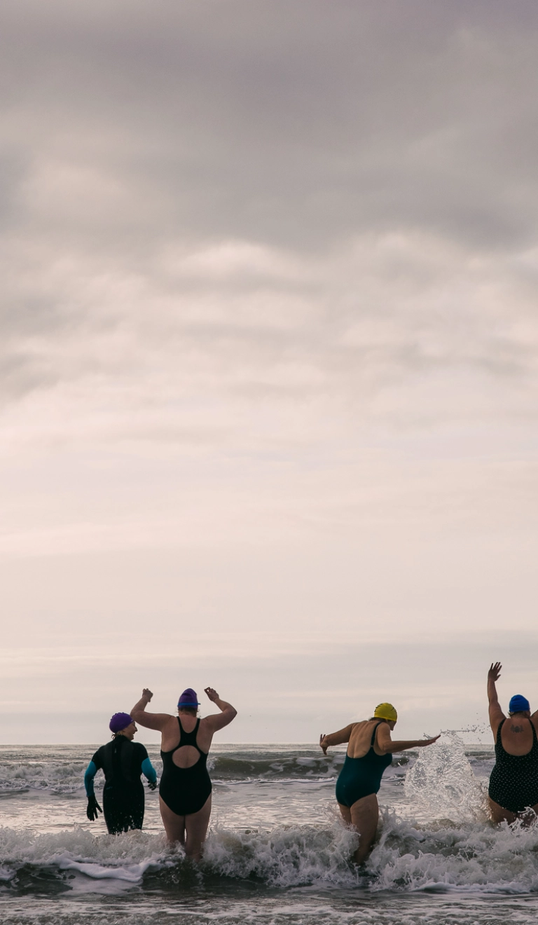 women in bathers running into the sea cheering and laughing