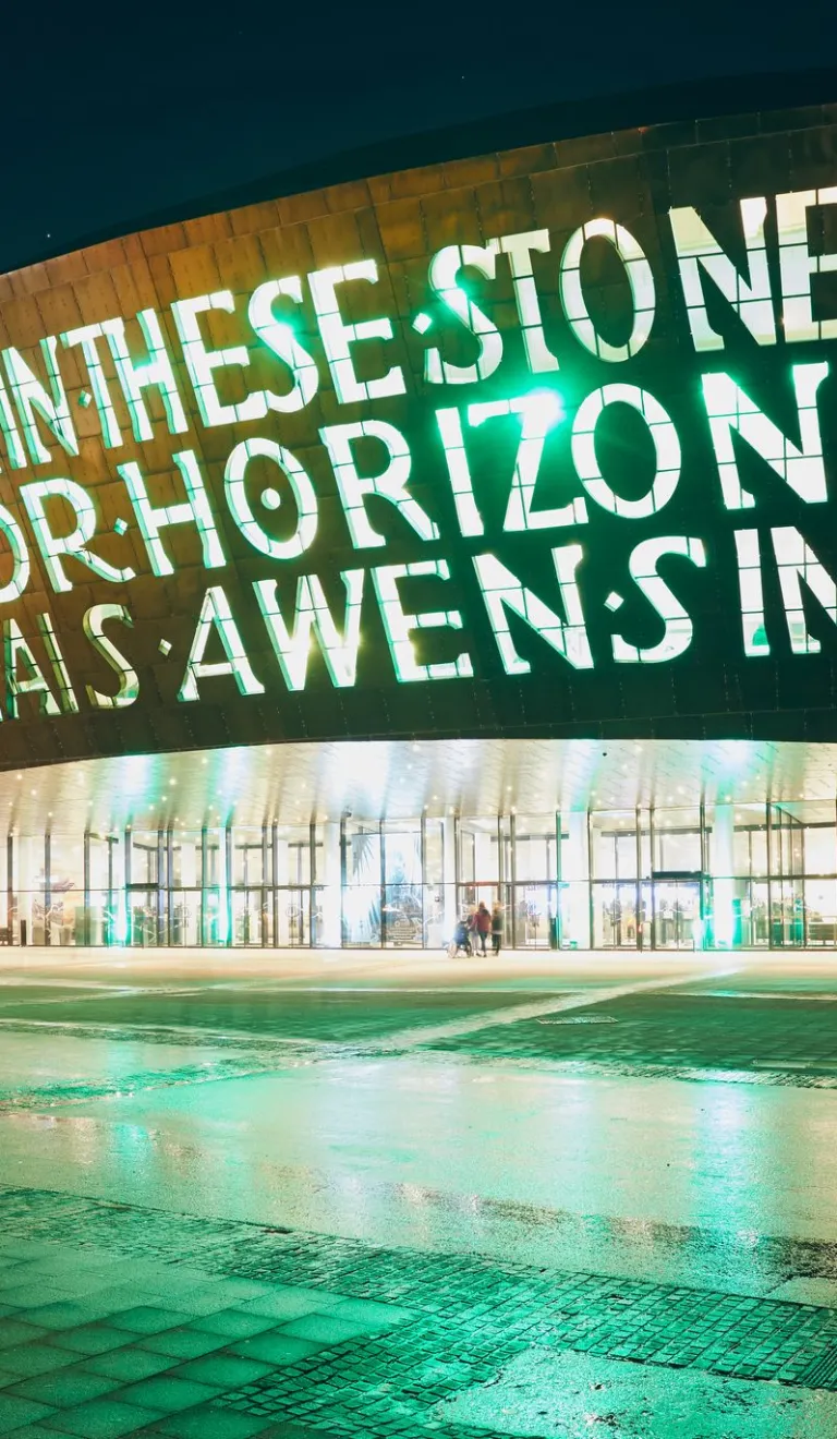 outsideof the wales millennium centre at night with words written into the building lit up 